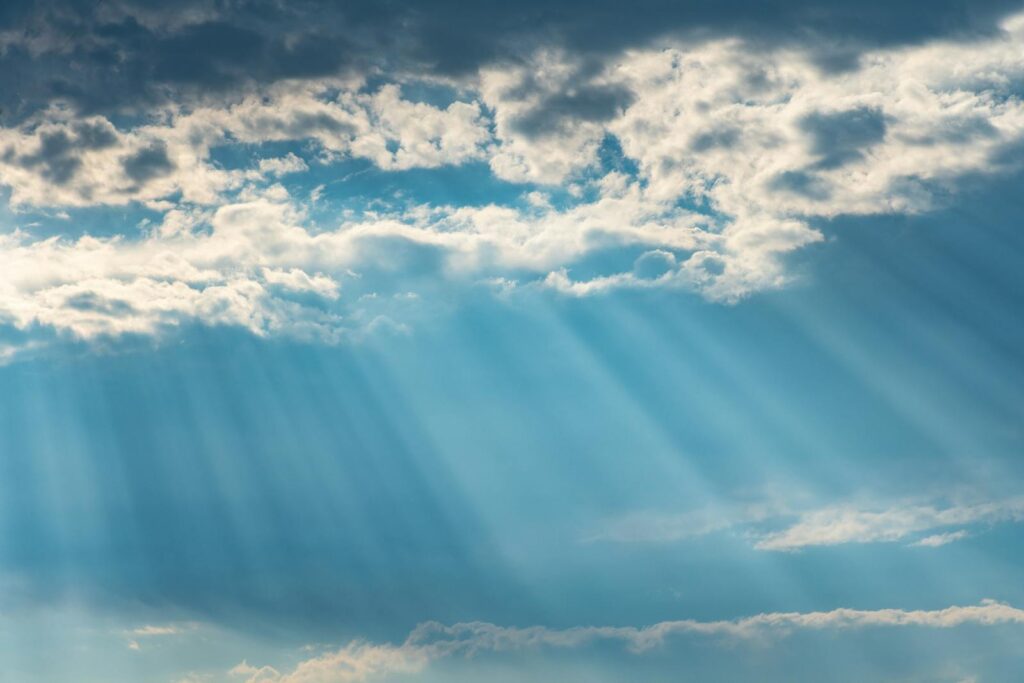 Vibrant sunrays pierce through a cloudy sky, creating a dramatic and dreamy cloudscape.