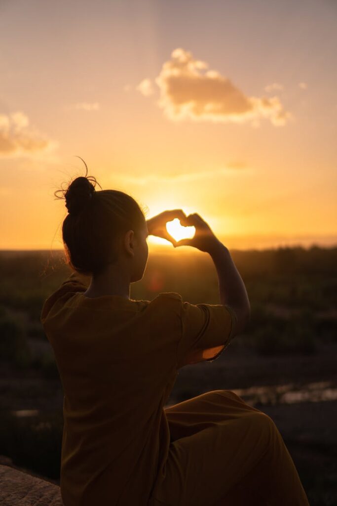 Silhouette of a person forming a heart with hands against a Morocco sunset.